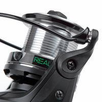 Close-up of a fishing reel with 'REAL' branding on a white background
